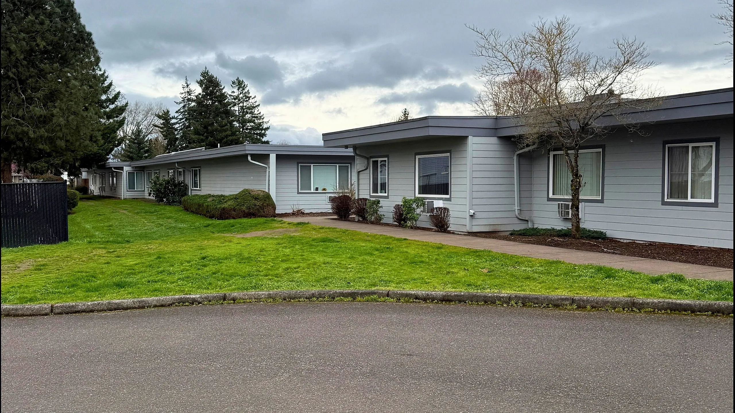 Charming one-story home with modern gray siding, nestled in a lush, green landscape under a cloudy sky.