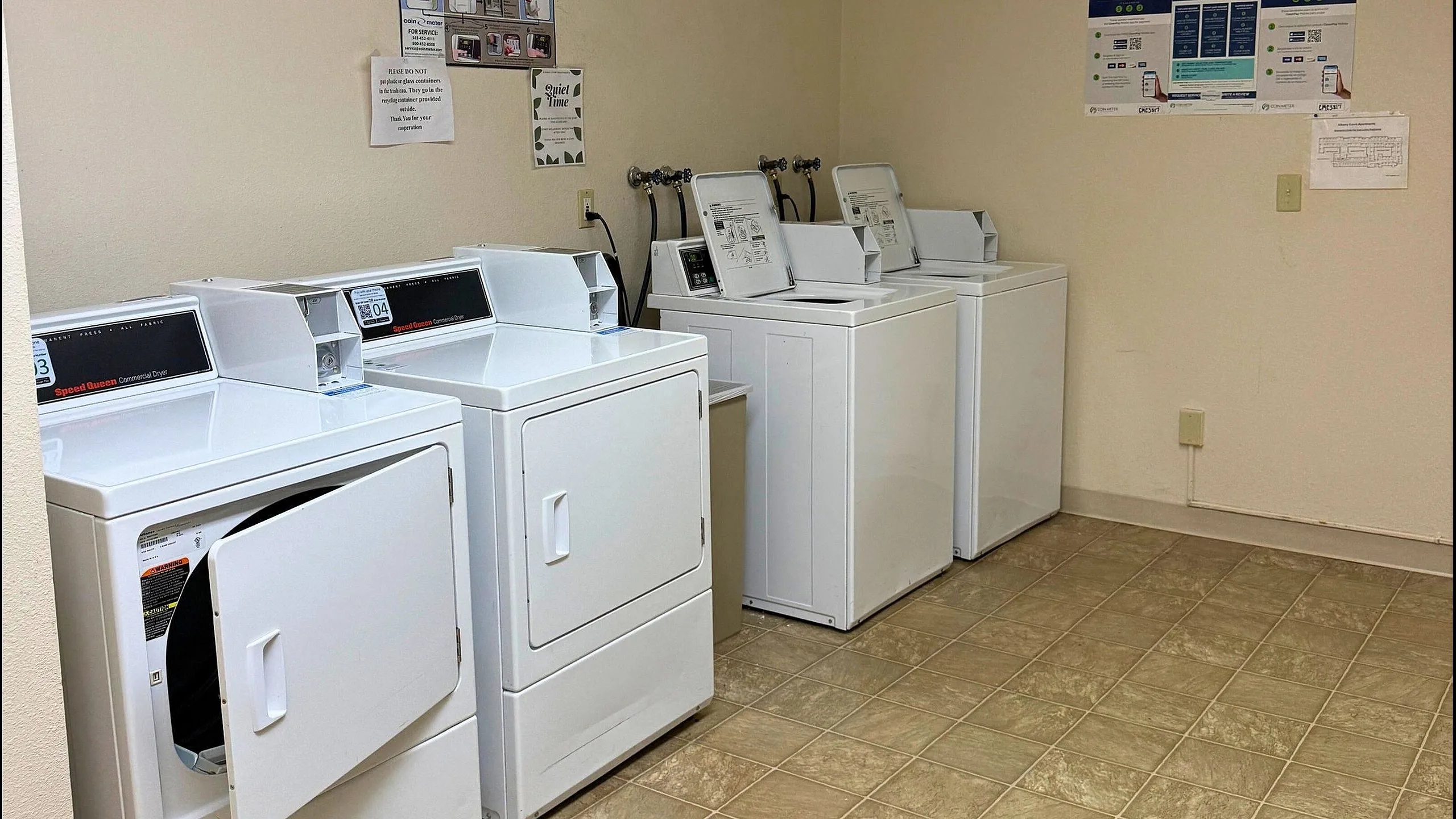 Bright and convenient laundry room featuring multiple washers and dryers with user-friendly controls.