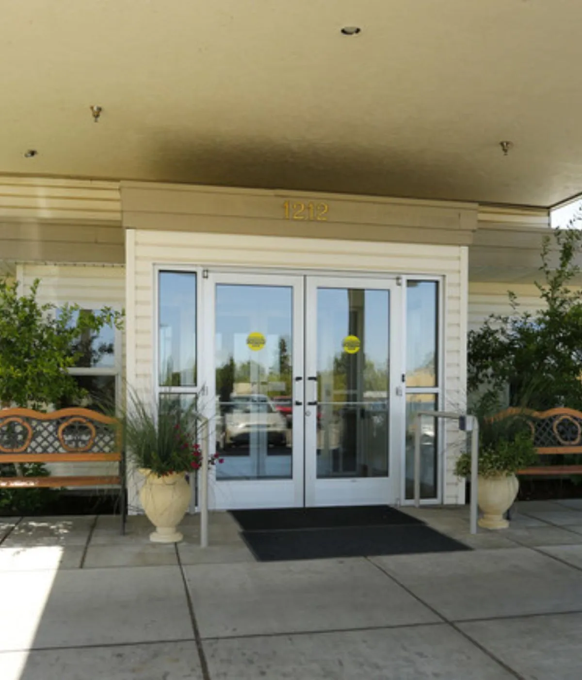 Elegant apartment entrance with glass doors, potted plants, and inviting benches at building 1212.