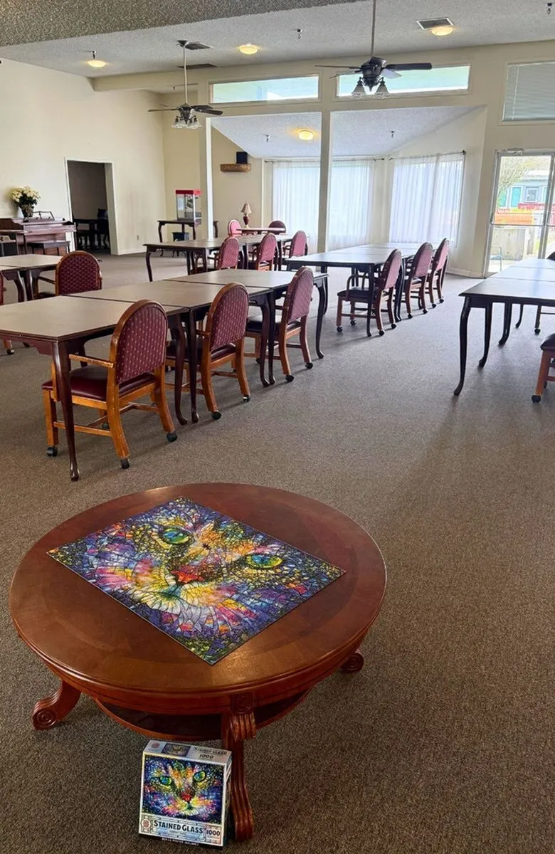 Spacious, elegant communal area with abundant natural light featuring multiple tables and chairs, complemented by a colorful stained glass artwork on a central round table.