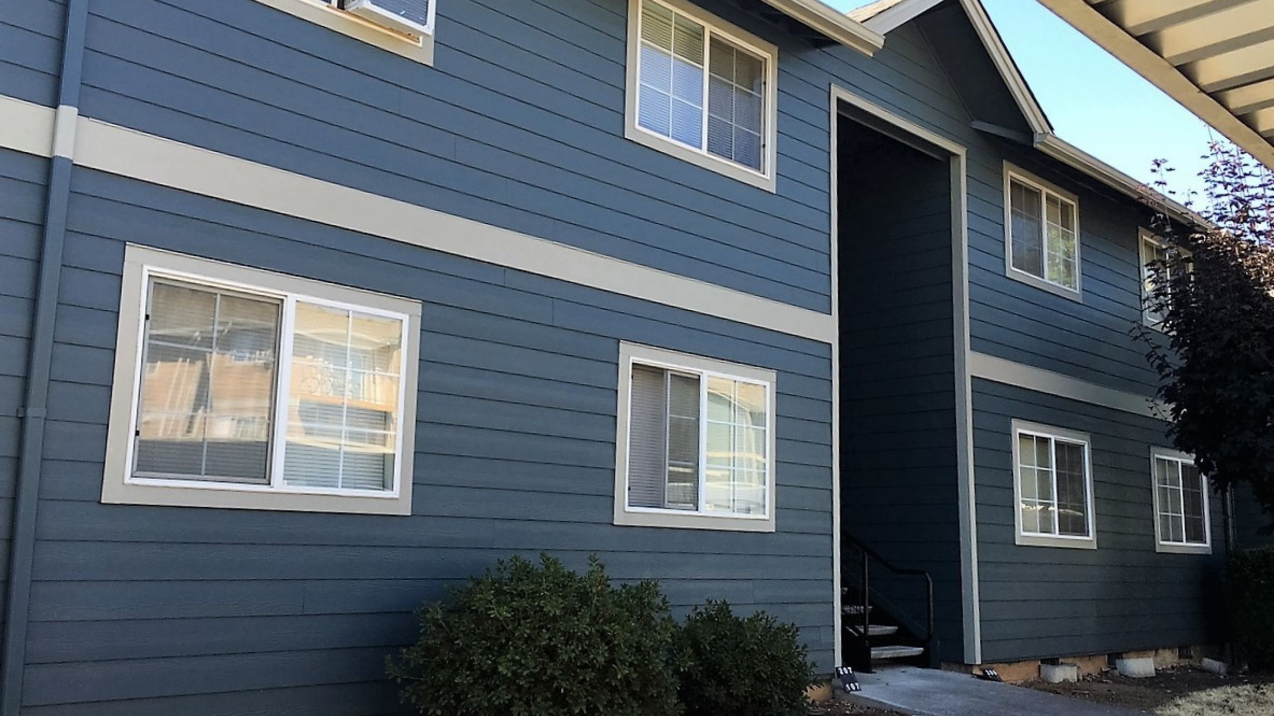 Charming blue apartment building with modern siding and large windows offering natural light, surrounded by well-maintained shrubs.