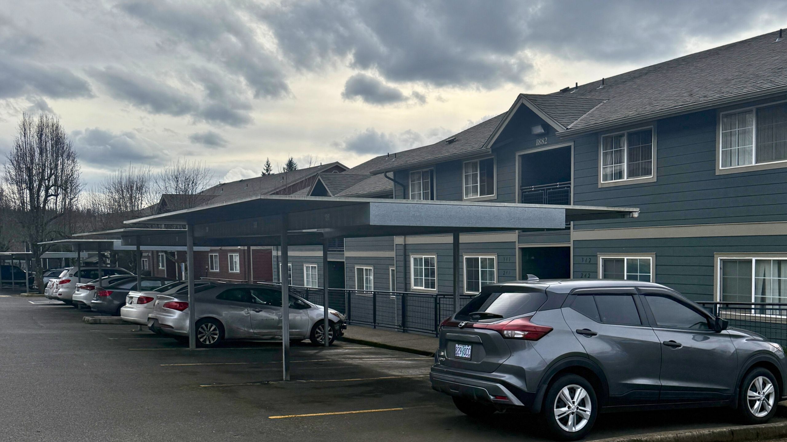 Charming apartment complex with ample covered parking and modern architecture, set against a serene overcast sky.