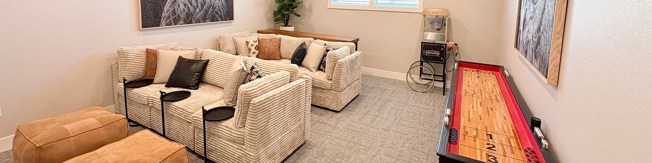 Modern entertainment room with plush sofas, a popcorn machine, and a sleek shuffleboard table, perfect for relaxation and fun.