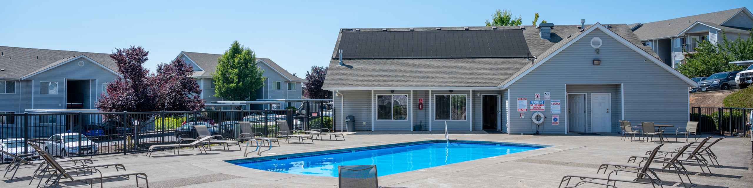 Inviting outdoor pool area with relaxing lounge chairs and modern clubhouse in a serene apartment community setting.