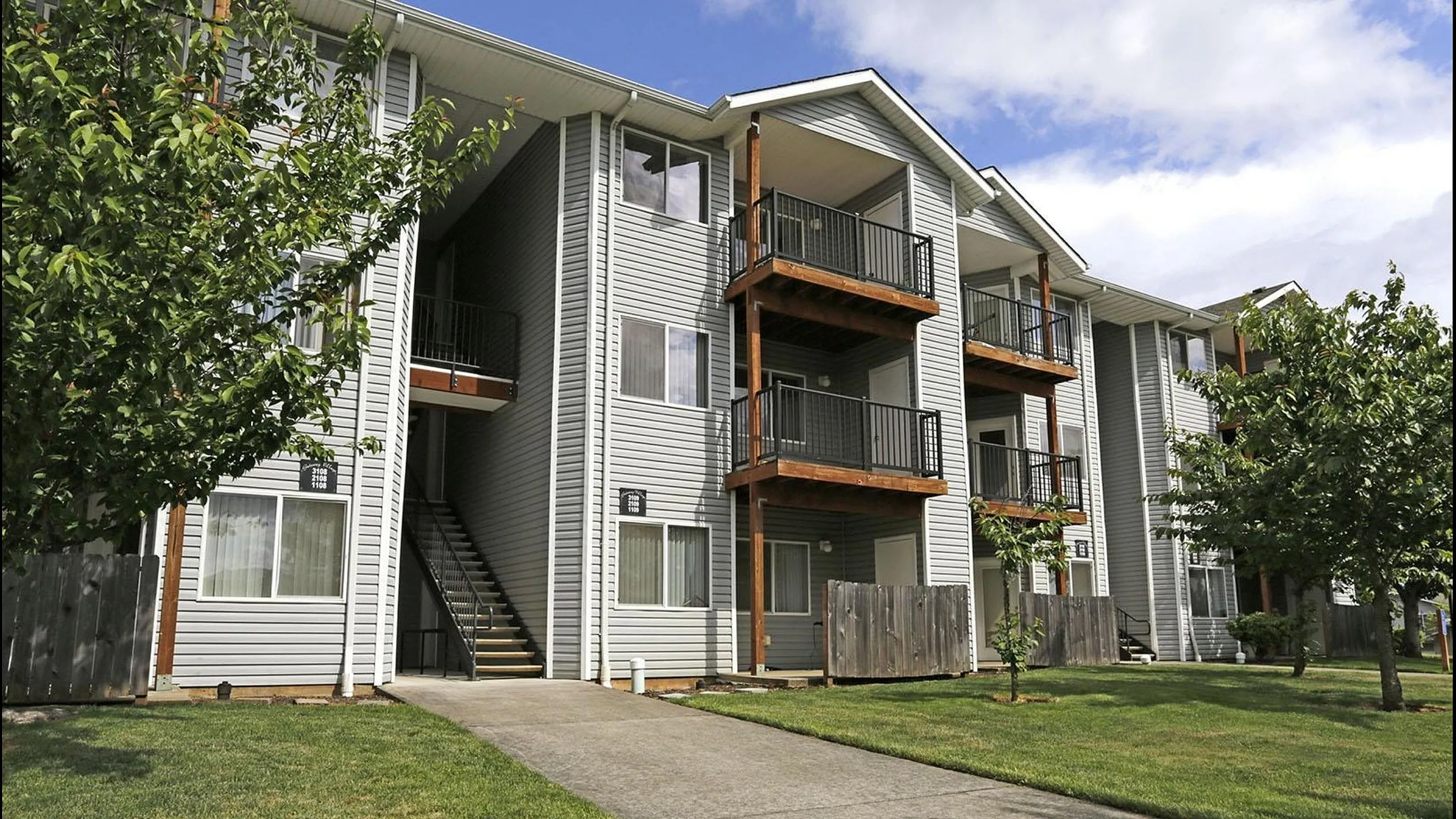 Charming multi-story apartment building with private balconies, surrounded by lush greenery and a serene pathway.