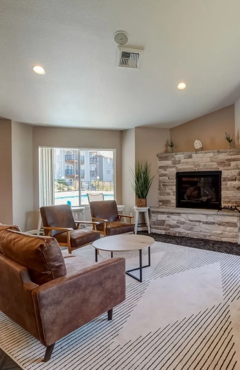Inviting living room with cozy leather furniture, a stone fireplace, large window with a view, and modern decor.