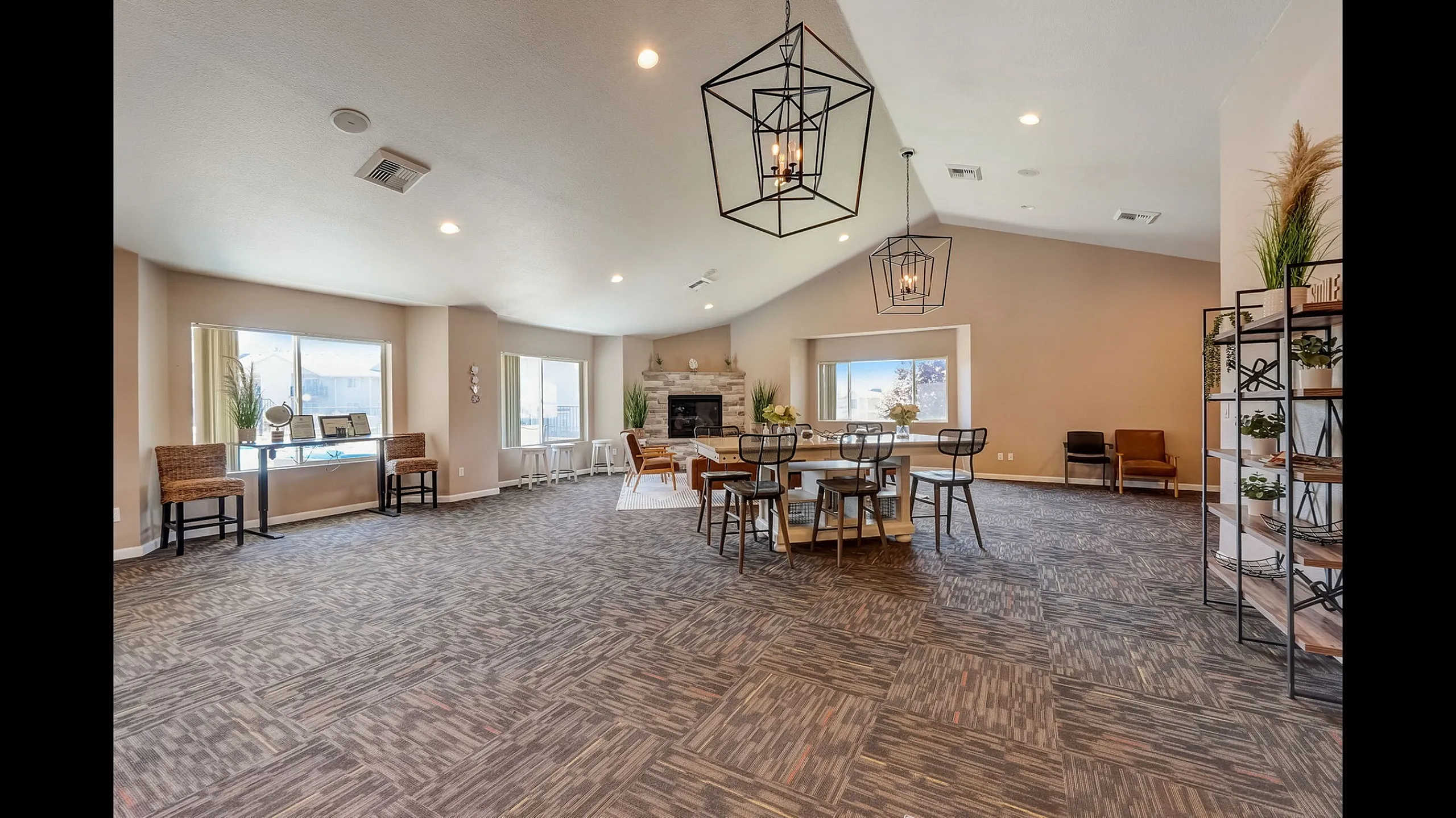 Elegant community room with modern chandeliers, cozy fireplace, and abundant natural light. Features stylish seating and lush greenery in a spacious layout.
