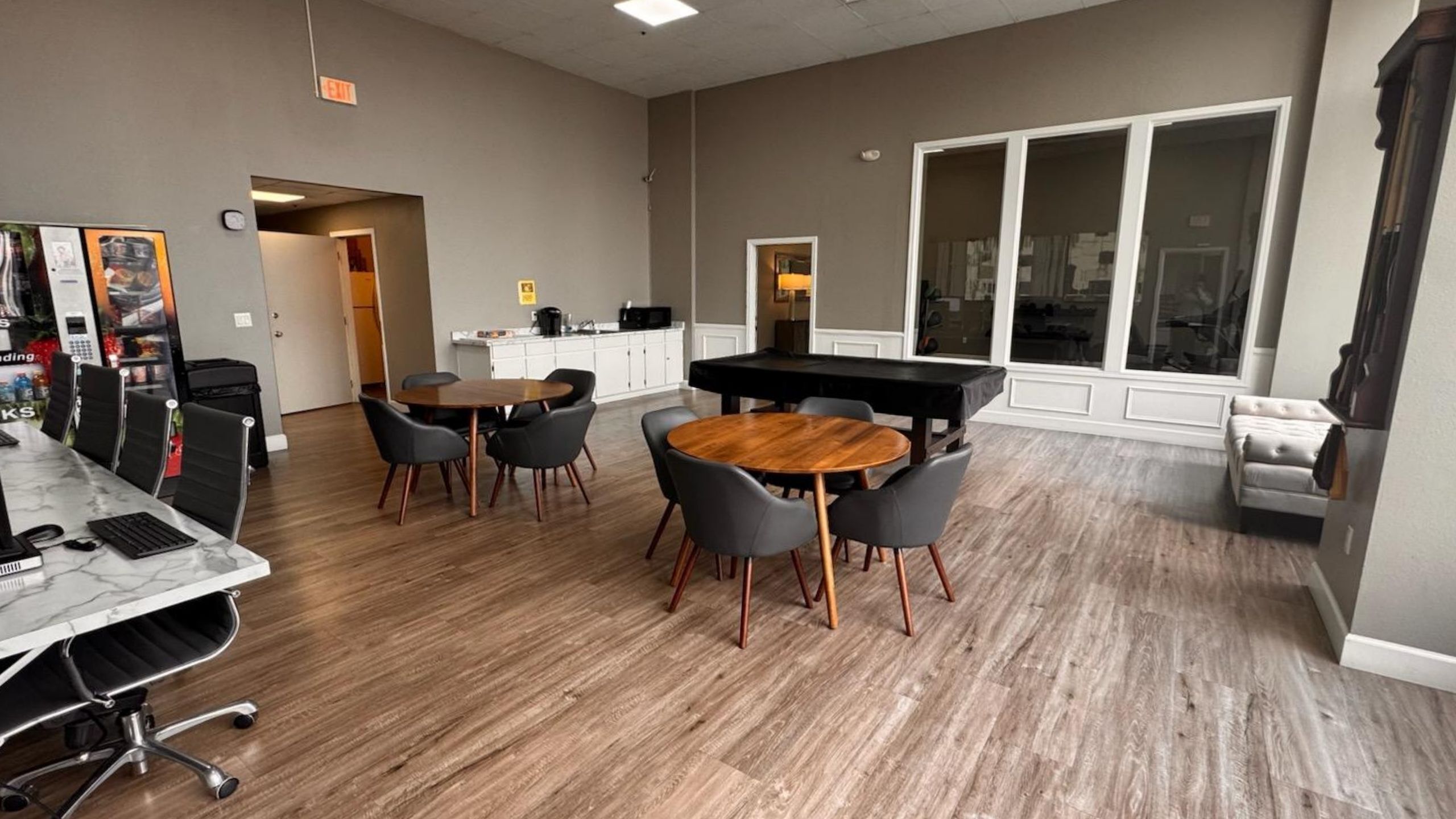 Elegant communal space with modern furniture, featuring round wooden tables, stylish chairs, and a sleek marble counter. Ideal for socializing or work meetings.