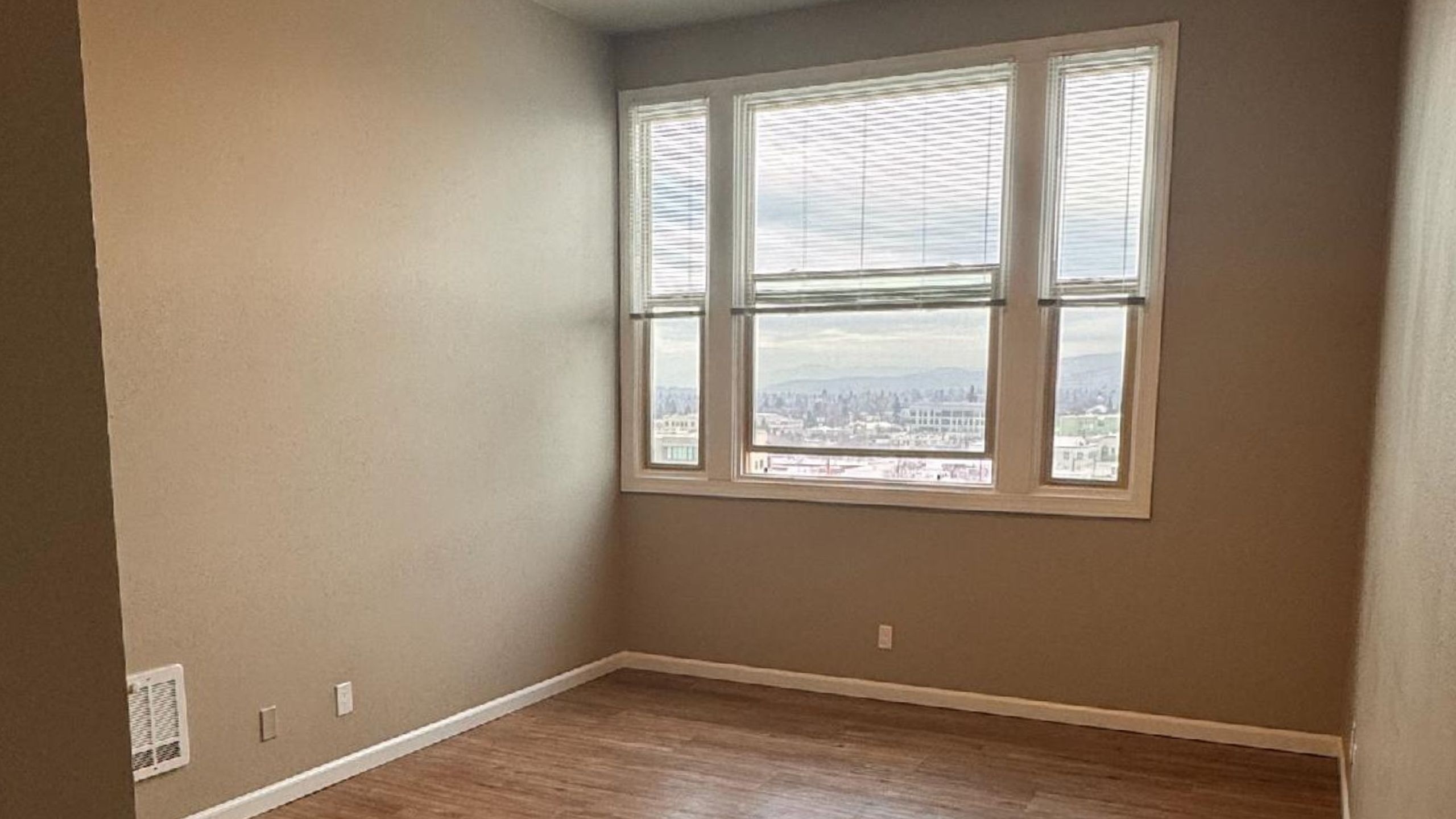Bright, empty room with large window offering panoramic city views and beautiful natural light highlights the inviting atmosphere.