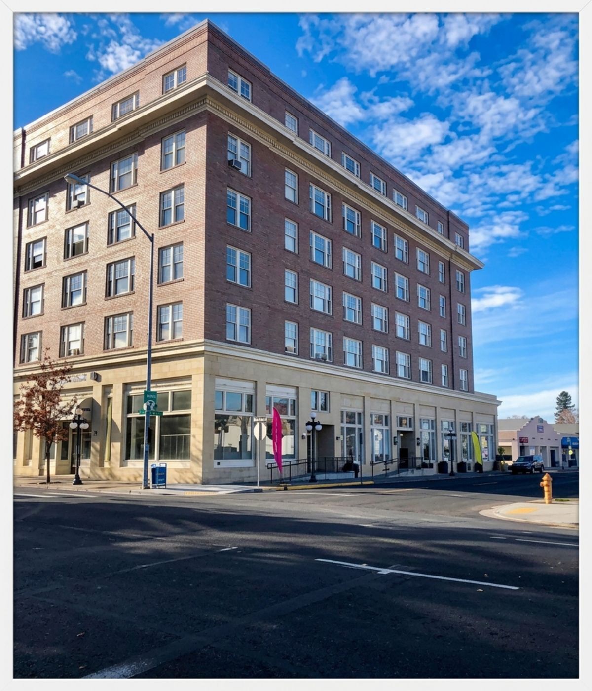 Charming historic apartment building with elegant brick facade and large windows, set against a vibrant blue sky and located on a bustling corner.