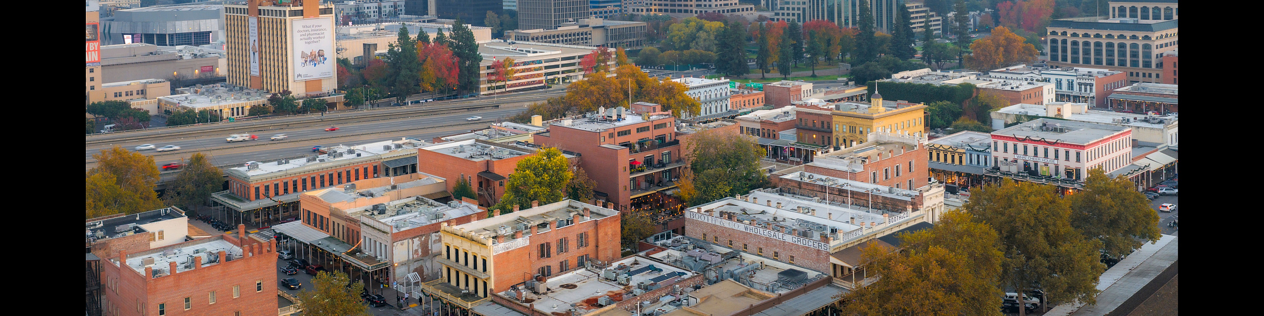 Breathtaking aerial view of a vibrant cityscape with modern skyscrapers, historic buildings, and lush tree-lined streets at sunset.