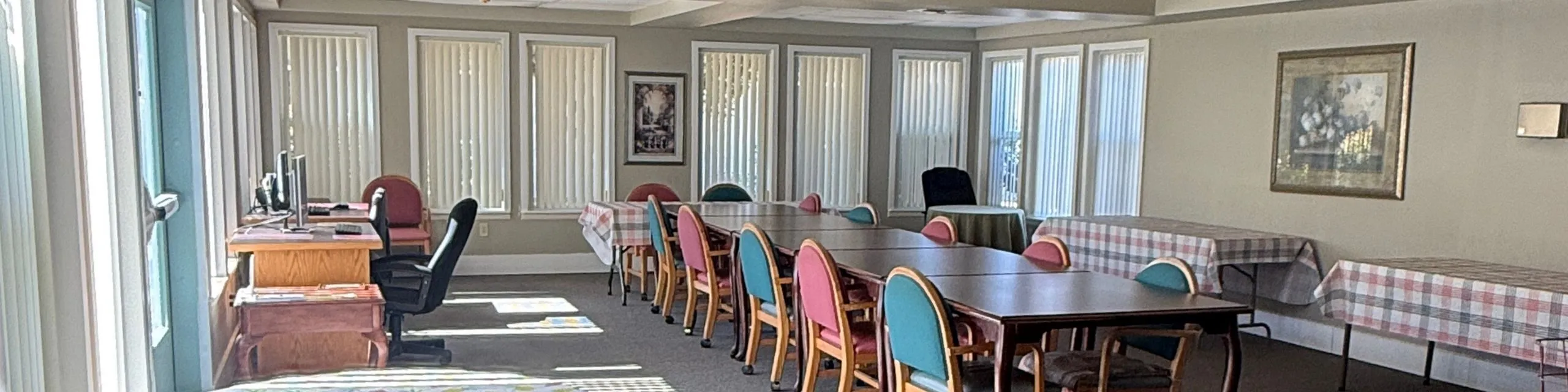 Bright and airy community room with large windows, multiple tables for gatherings, and vibrant chairs, perfect for events and meetings.