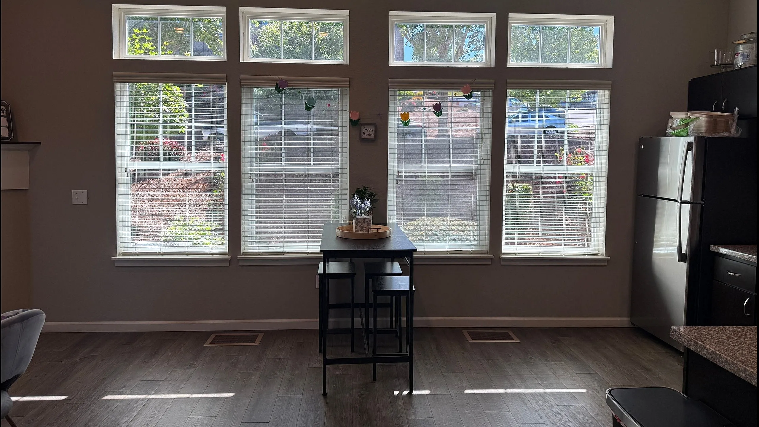 Bright apartment dining area with large windows, modern decor, and a sleek kitchen with stainless steel appliances.