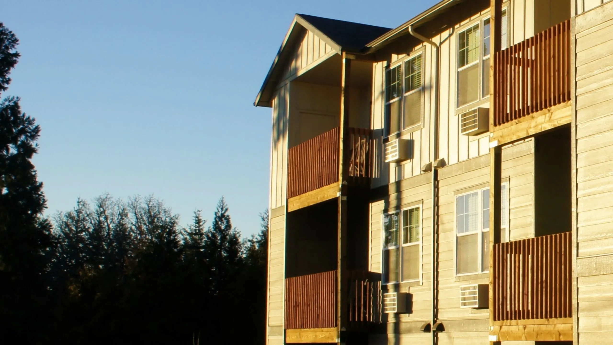 Charming apartment exterior with sunlit balconies and a scenic treetop backdrop.