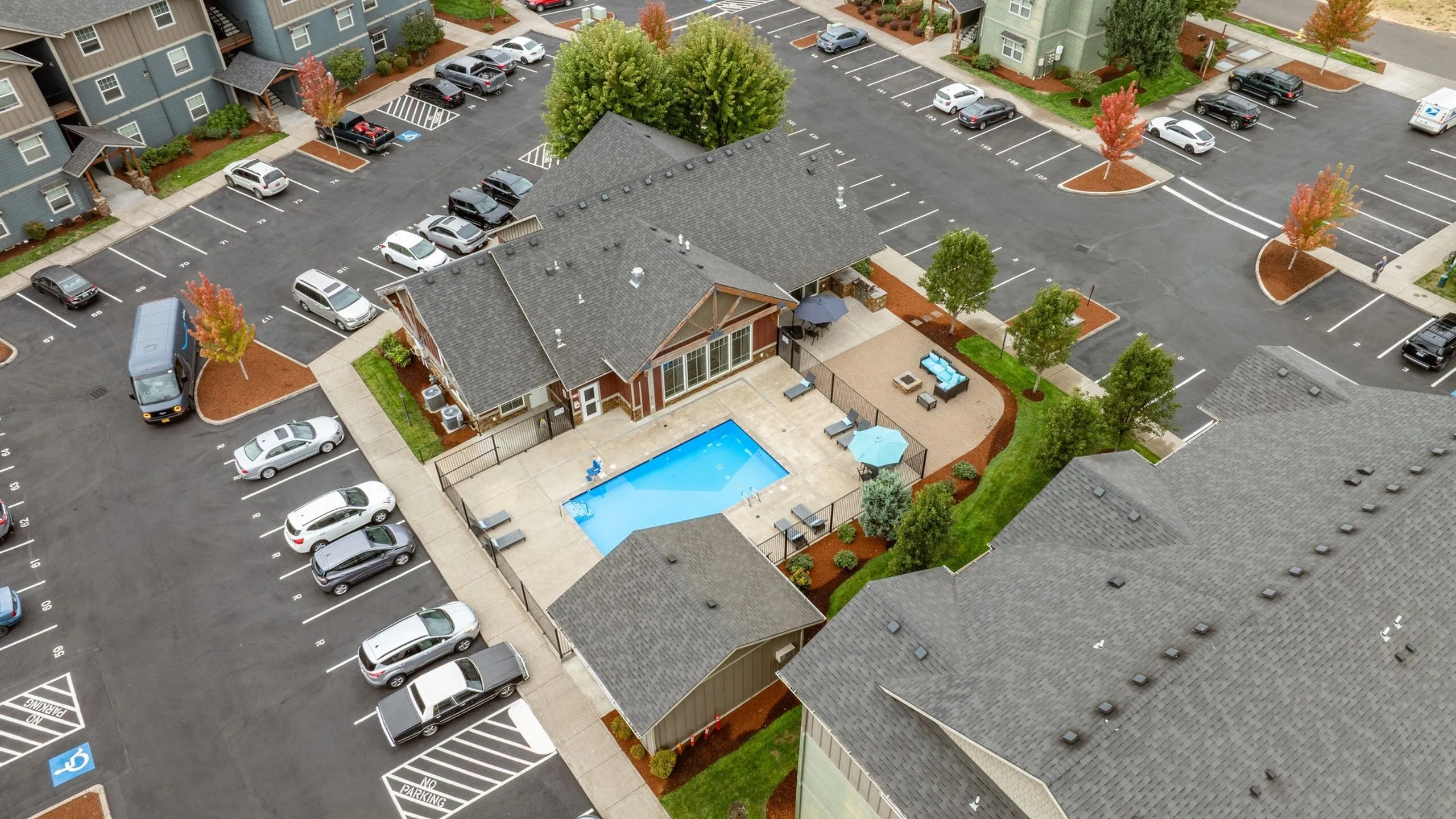 Aerial view of a charming apartment complex featuring a central swimming pool, ample parking, and lush landscaping for a vibrant living experience.