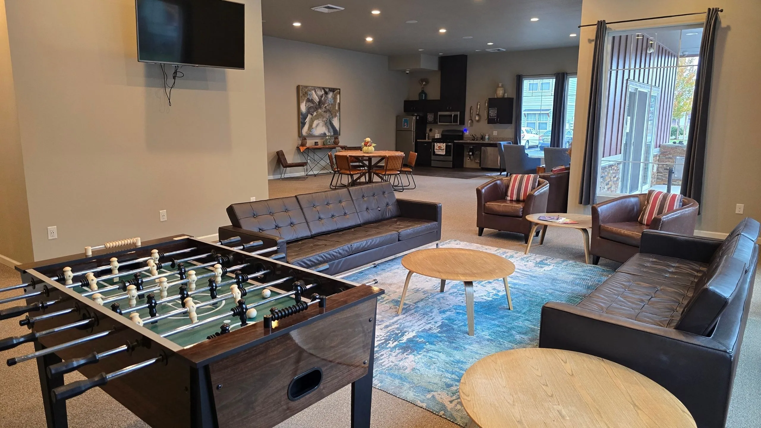 Contemporary apartment lounge showcasing a sleek foosball table, modern leather seating, vibrant rug, and an open kitchen layout with dining area.