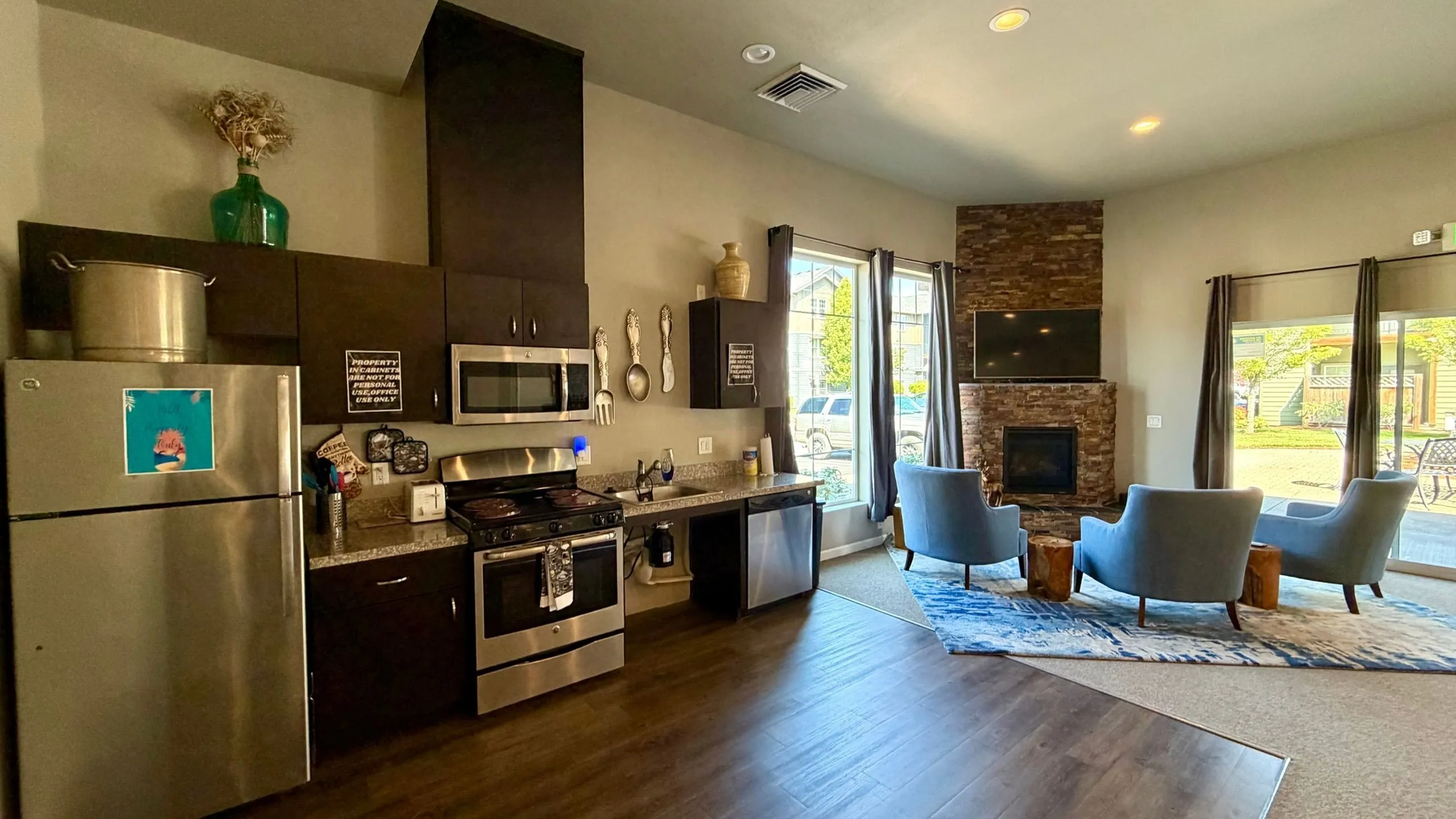 Modern open-concept kitchen and living room with sleek appliances, cozy stone fireplace, and large windows revealing outdoor views.