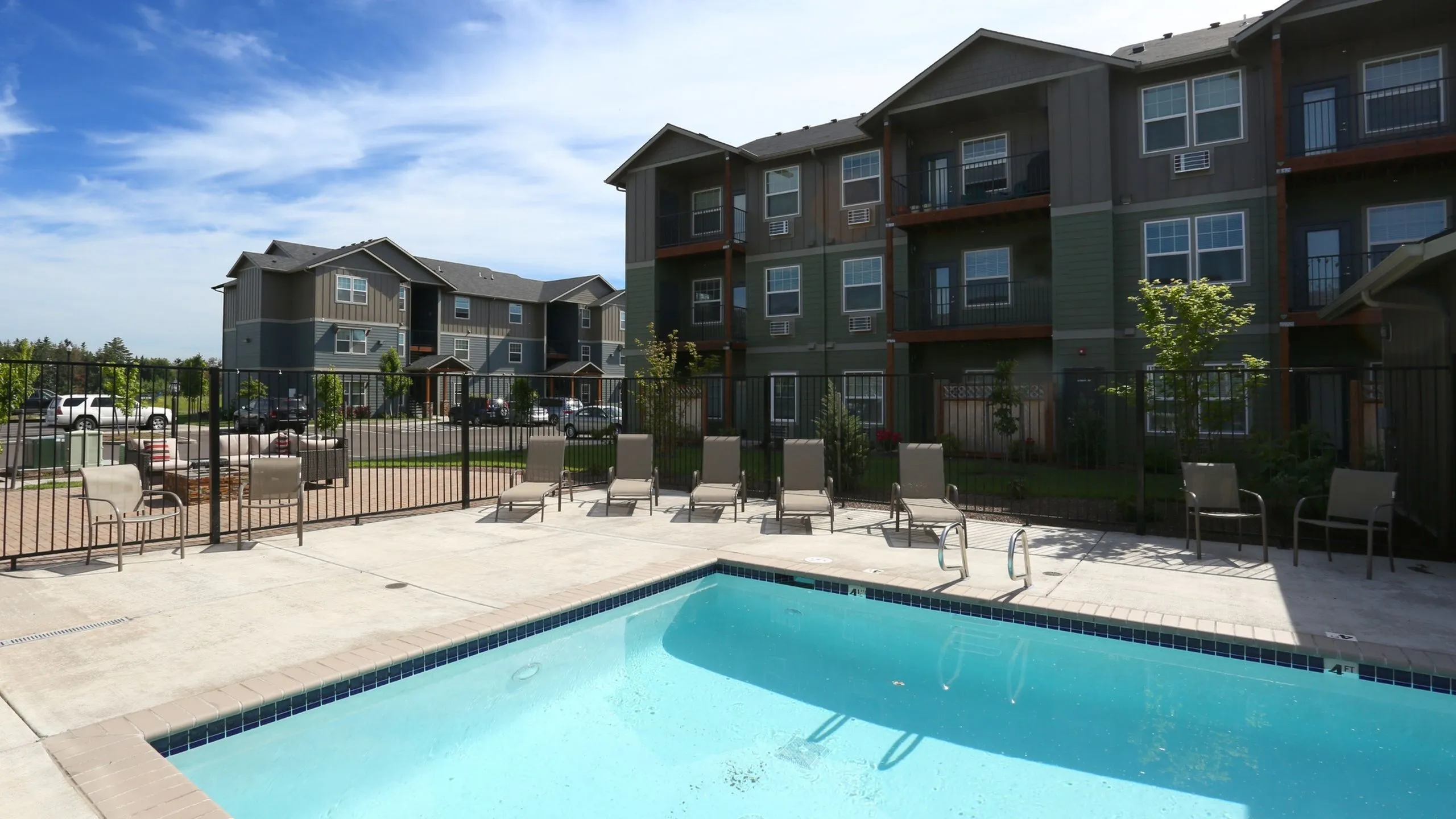 Inviting apartment complex with modern balconies overlooking a sparkling swimming pool and sunlit patio area.