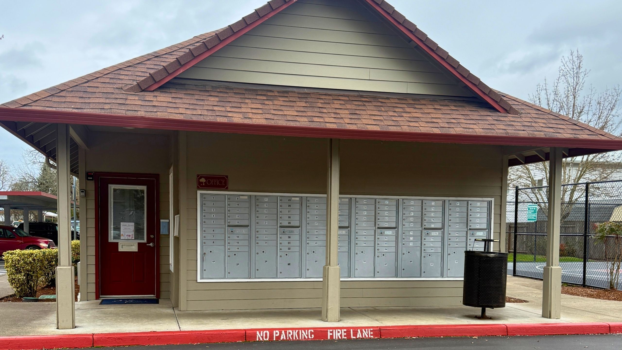 Quaint community office with a charming red door and convenient mailboxes, nestled in a serene neighborhood setting.