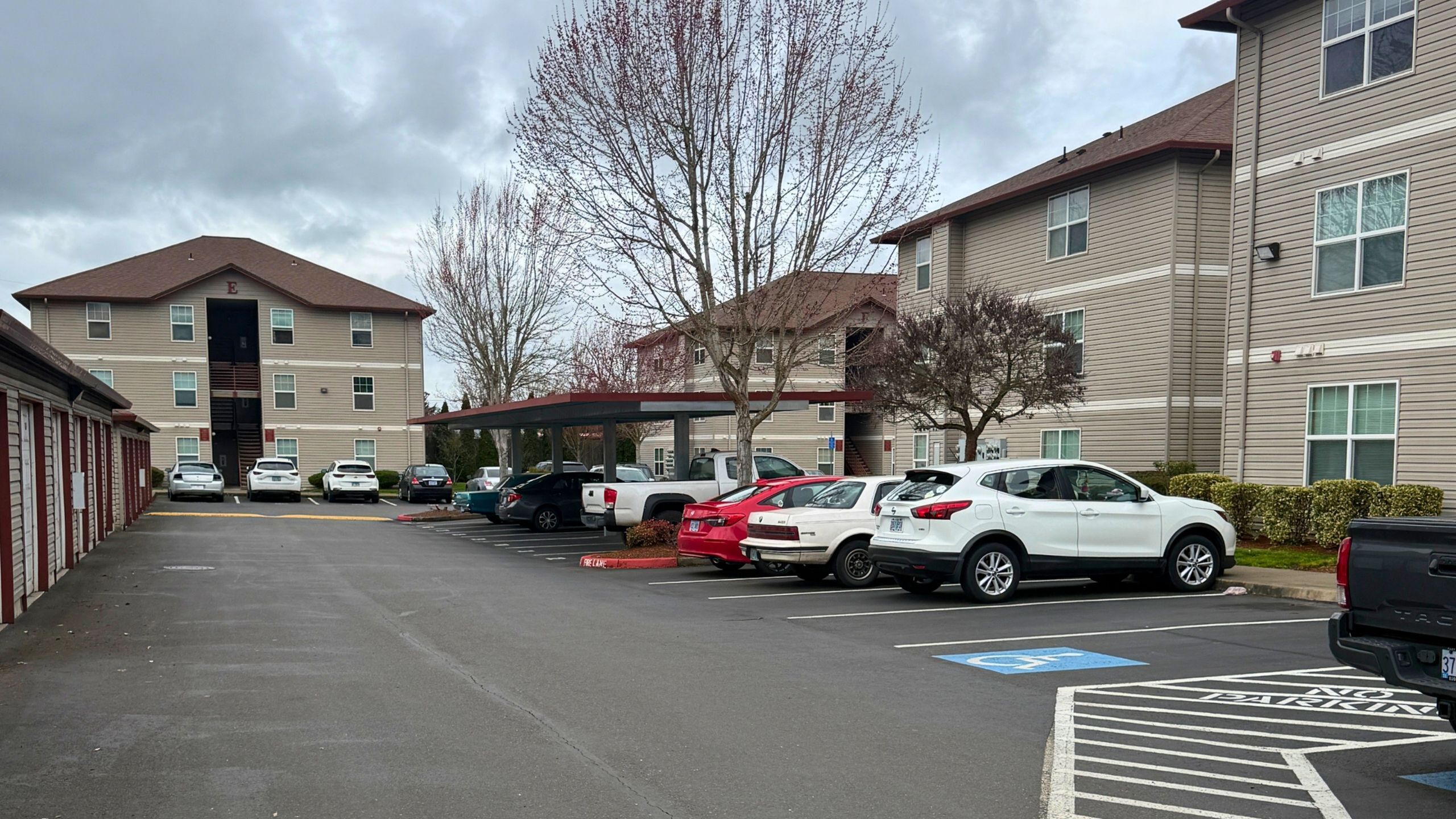 Charming residential complex with spacious parking area and modern exterior, surrounded by lush greenery and serene trees.