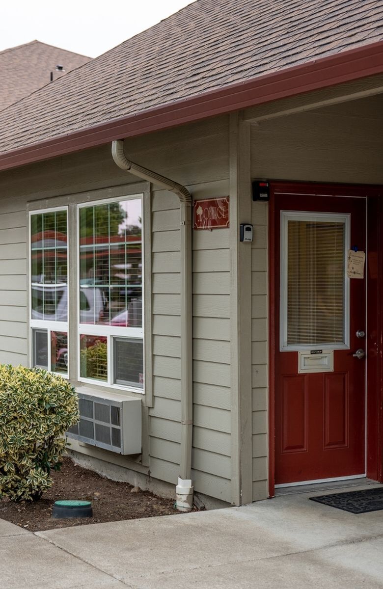 Charming exterior of a leasing office with a welcoming red door and lush greenery, offering a cozy and approachable atmosphere.