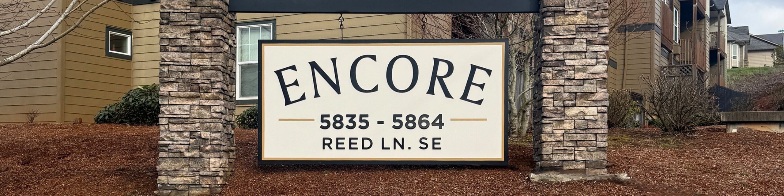 Inviting entrance sign for Encore apartments on Reed Lane, surrounded by charming brickwork and lush greenery.