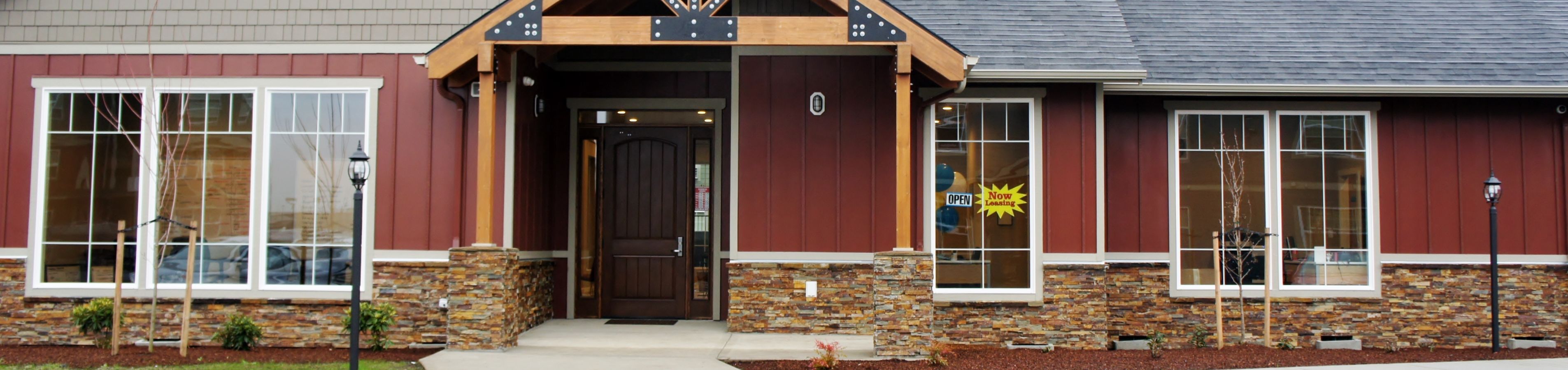 Charming building entrance with rustic stonework and expansive windows, welcoming with 'Now Leasing' sign.