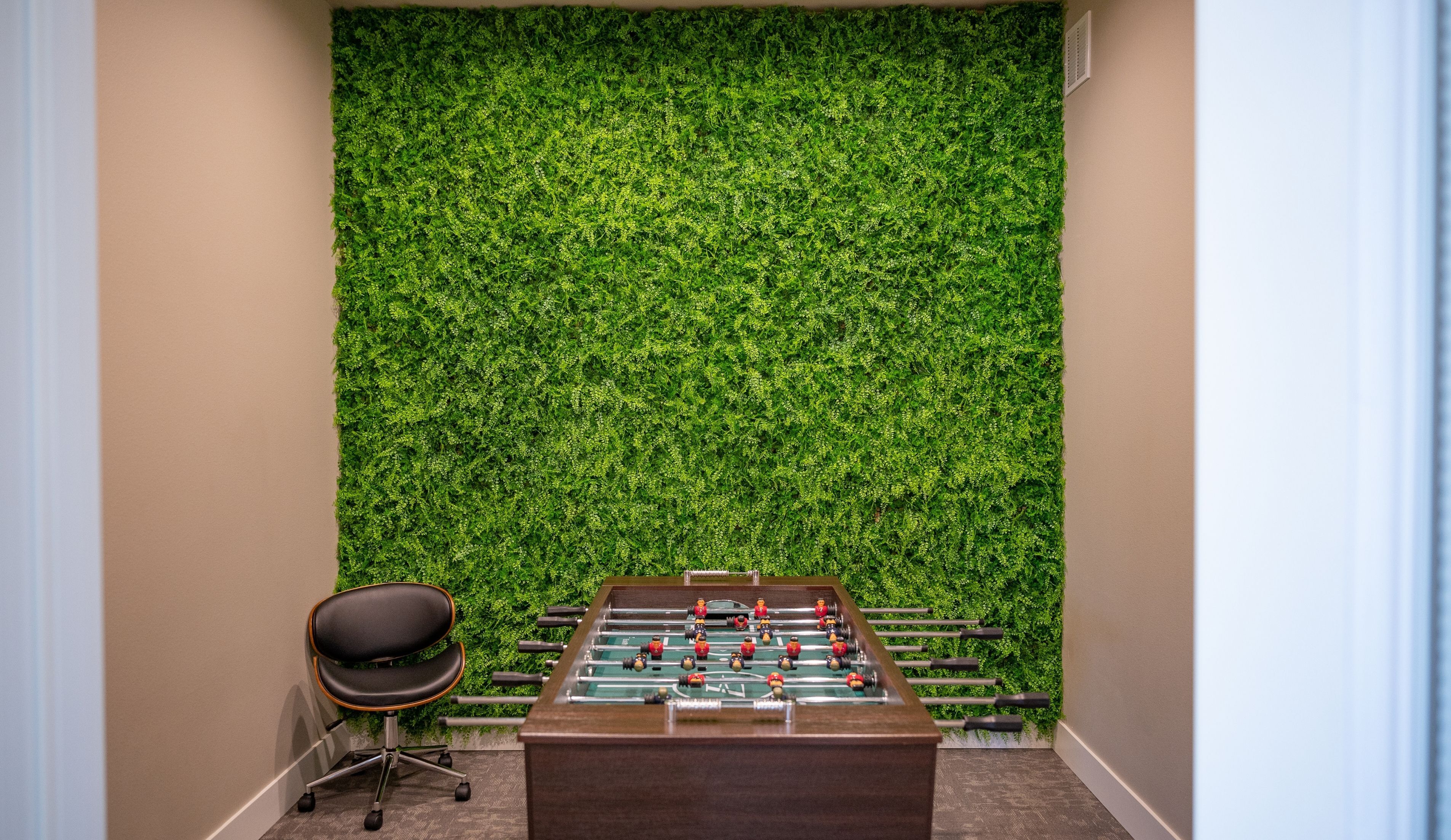 Inviting game room with a modern foosball table and vibrant green wall, perfect for leisure and relaxation.