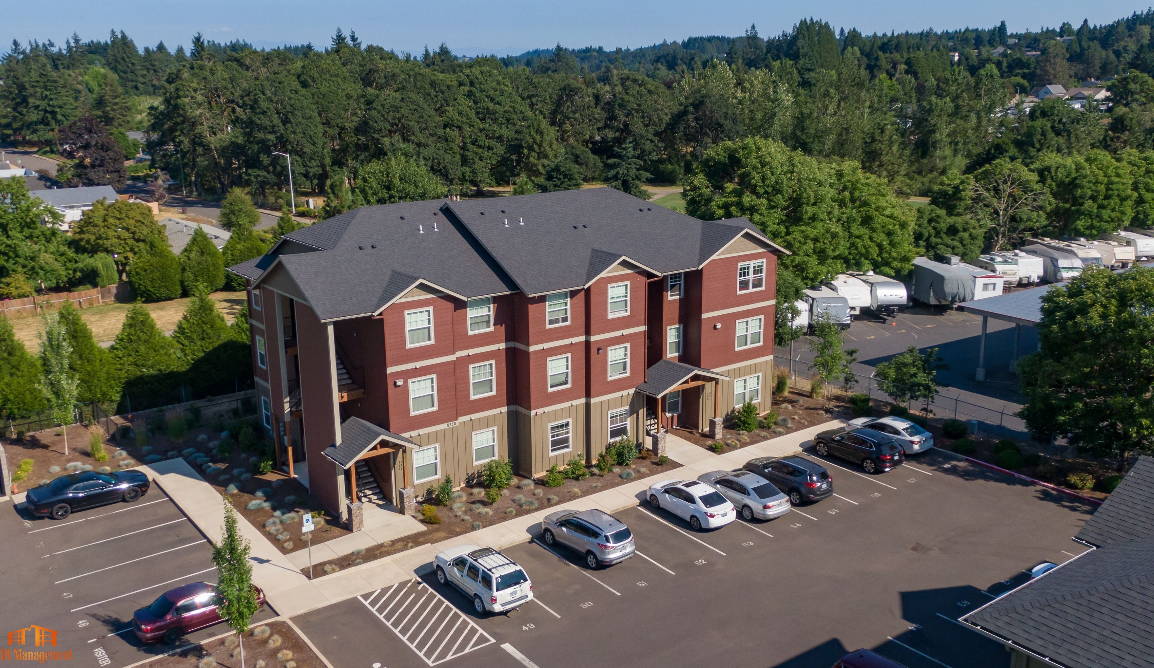 Charming multi-story apartment building with a spacious parking lot, surrounded by lush greenery.