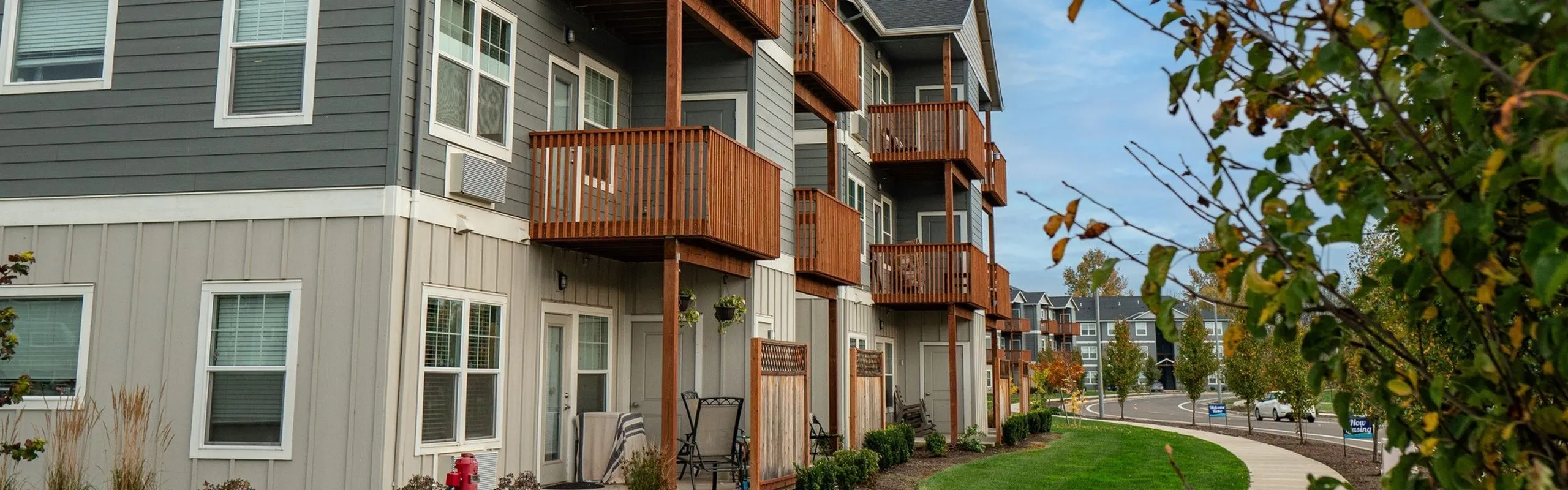 Modern apartment building with private balconies and lush greenery in a peaceful neighborhood setting.