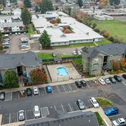 Charming aerial view of an apartment complex featuring a central swimming pool, surrounded by lush greenery and ample parking space.
