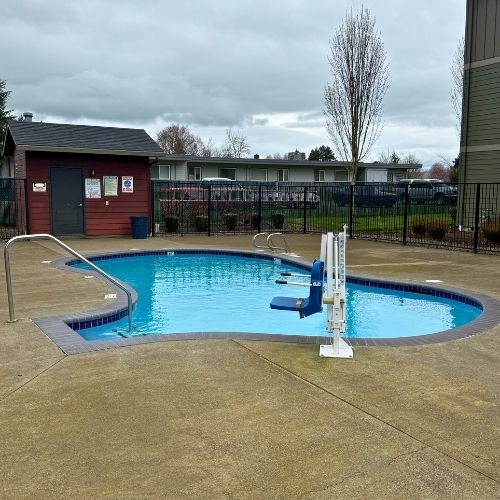 Inviting outdoor swimming pool area with a modern accessibility lift, surrounded by a spacious patio and charming community garden views.