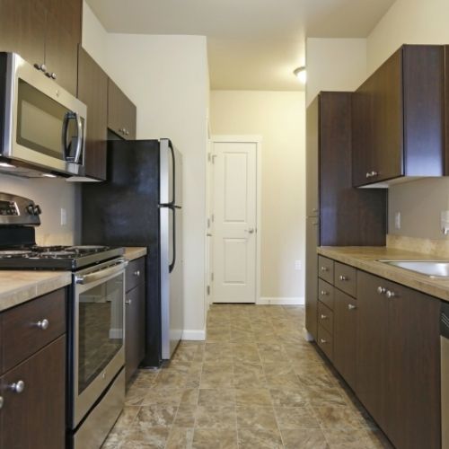 Modern kitchen with sleek dark wood cabinets, stainless steel appliances, and elegant tile flooring.