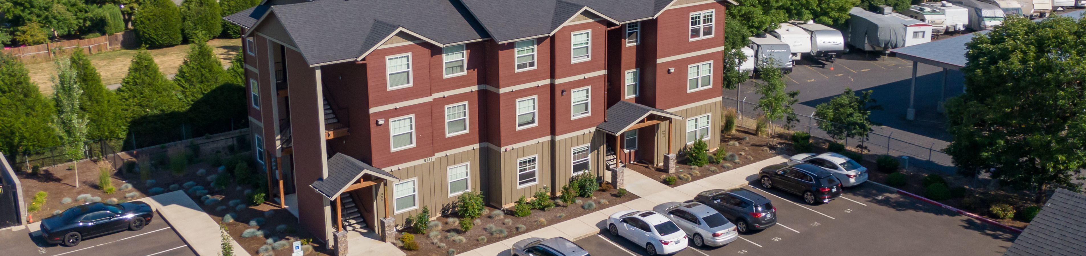 Charming three-story apartment building with modern design, ample parking, and lush greenery surroundings.