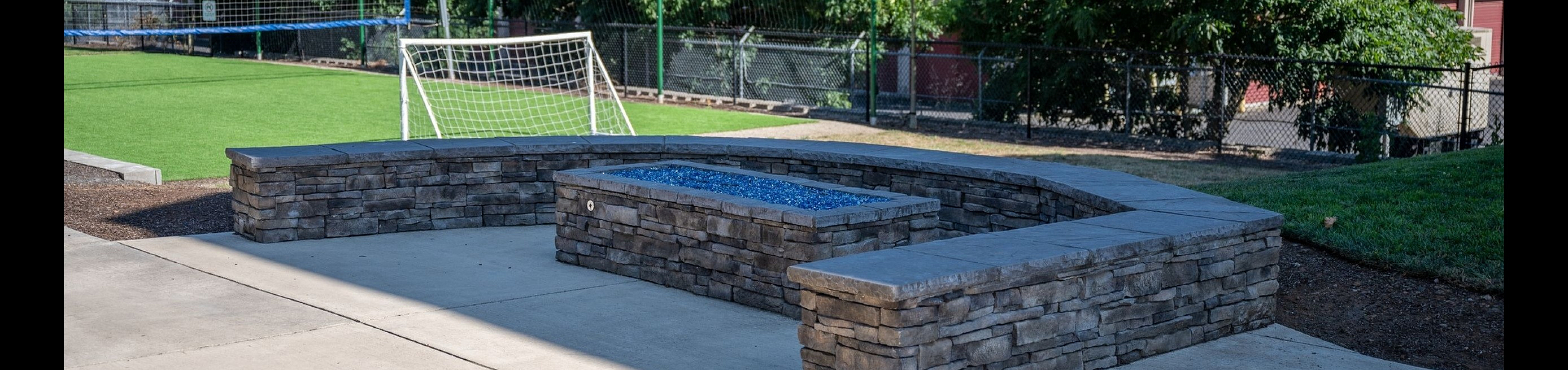 Inviting outdoor space featuring a stylish stone fire pit and a lush green soccer field in the background, perfect for relaxation and recreation.