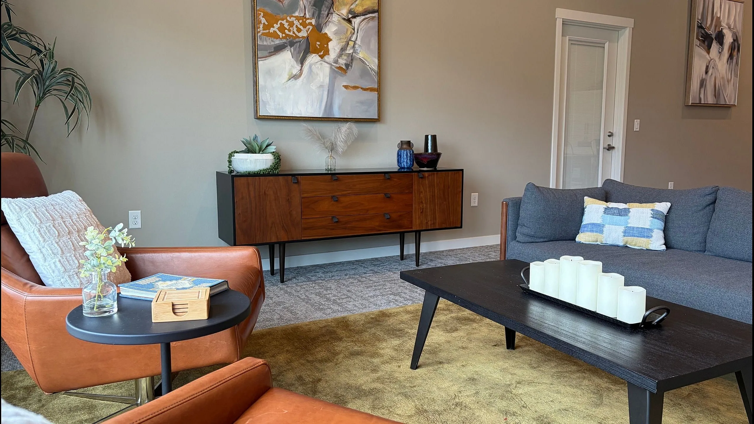 Chic living room with modern decor, featuring a stylish gray sofa, leather armchairs, and a sleek wooden console. Contemporary art and lush plants add elegance to the inviting space.