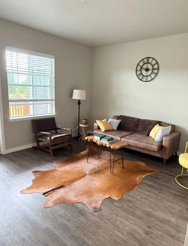 Inviting living room featuring a modern sofa, stylish decor, and a warm cowhide rug, creating a cozy ambiance with ample natural light.