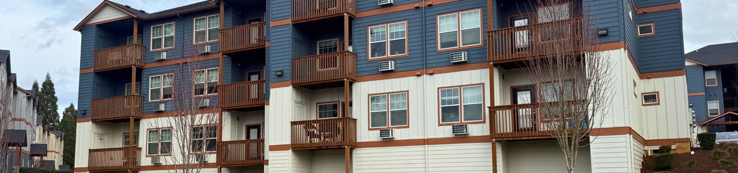 Charming multi-story apartment complex with wooden balconies and a modern architectural design, surrounded by lush greenery and a peaceful neighborhood setting.