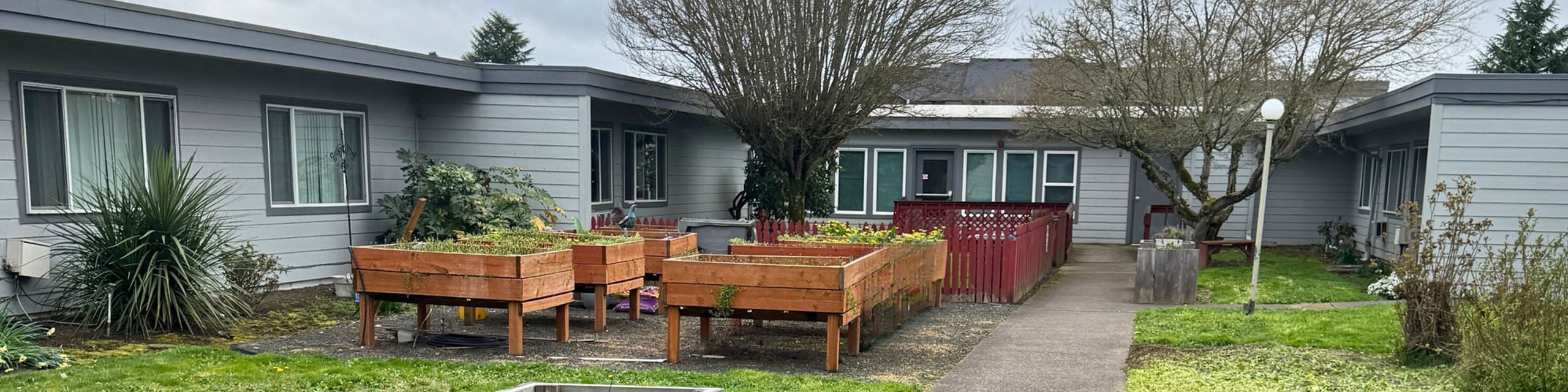Charming single-story apartment complex featuring a community garden with raised planters and lush greenery.