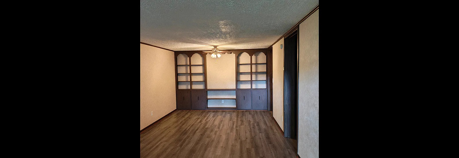 Elegant living room with rich vinyl plank flooring and built-in shelving, complemented by a warm ceiling light.