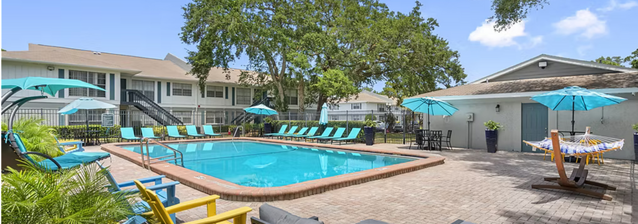 Inviting outdoor pool area with vibrant lounge chairs, blue umbrellas, and lush greenery, offering a relaxing and tropical atmosphere.