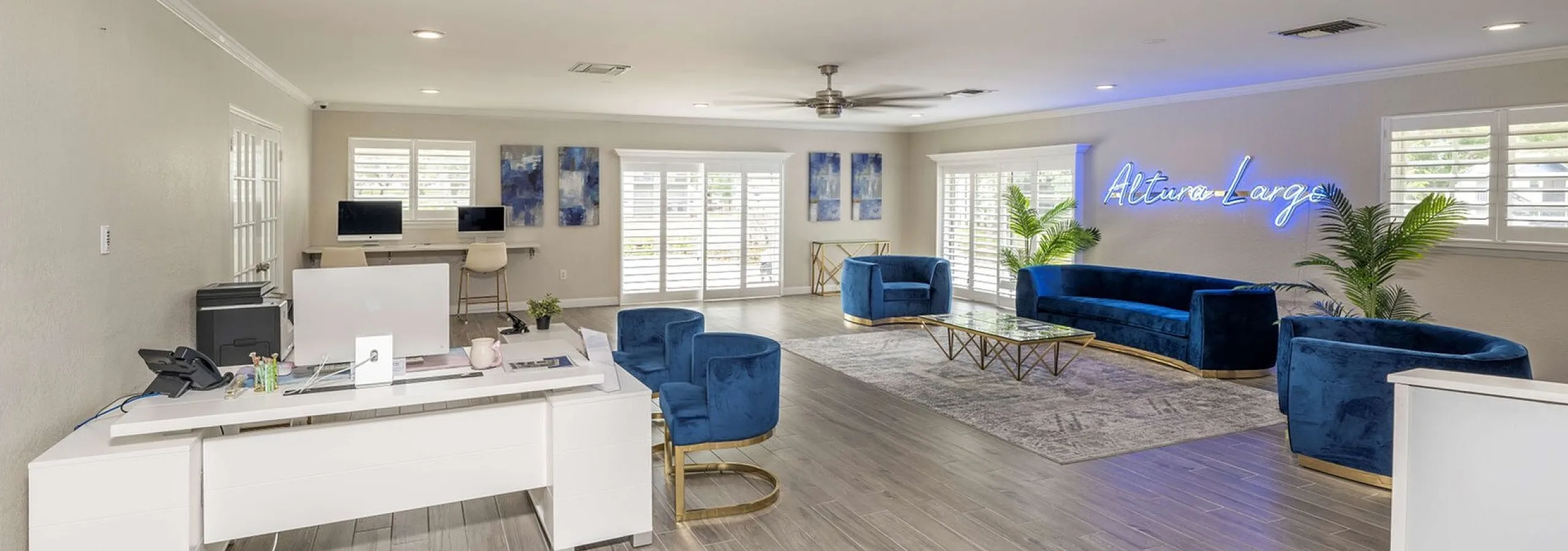 Spacious modern lounge with chic blue velvet seating, contemporary decor, and ample natural light, featuring a stylish workspace and vibrant ambiance.