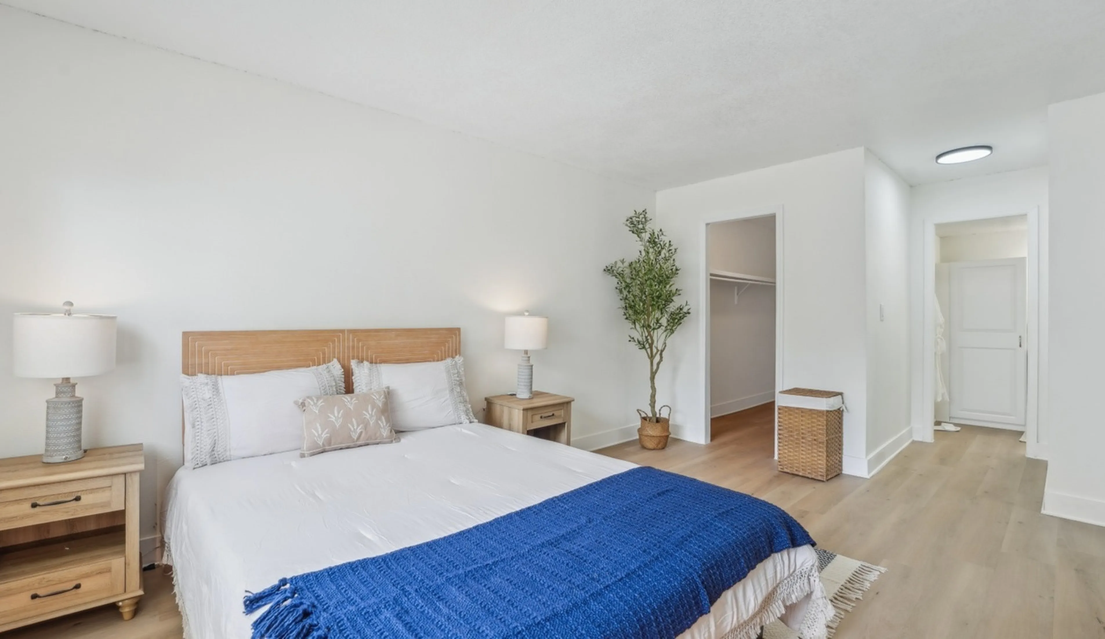 Bright, inviting bedroom with a cozy wooden bed frame, lush plant, and stylish decor for a tranquil living experience.