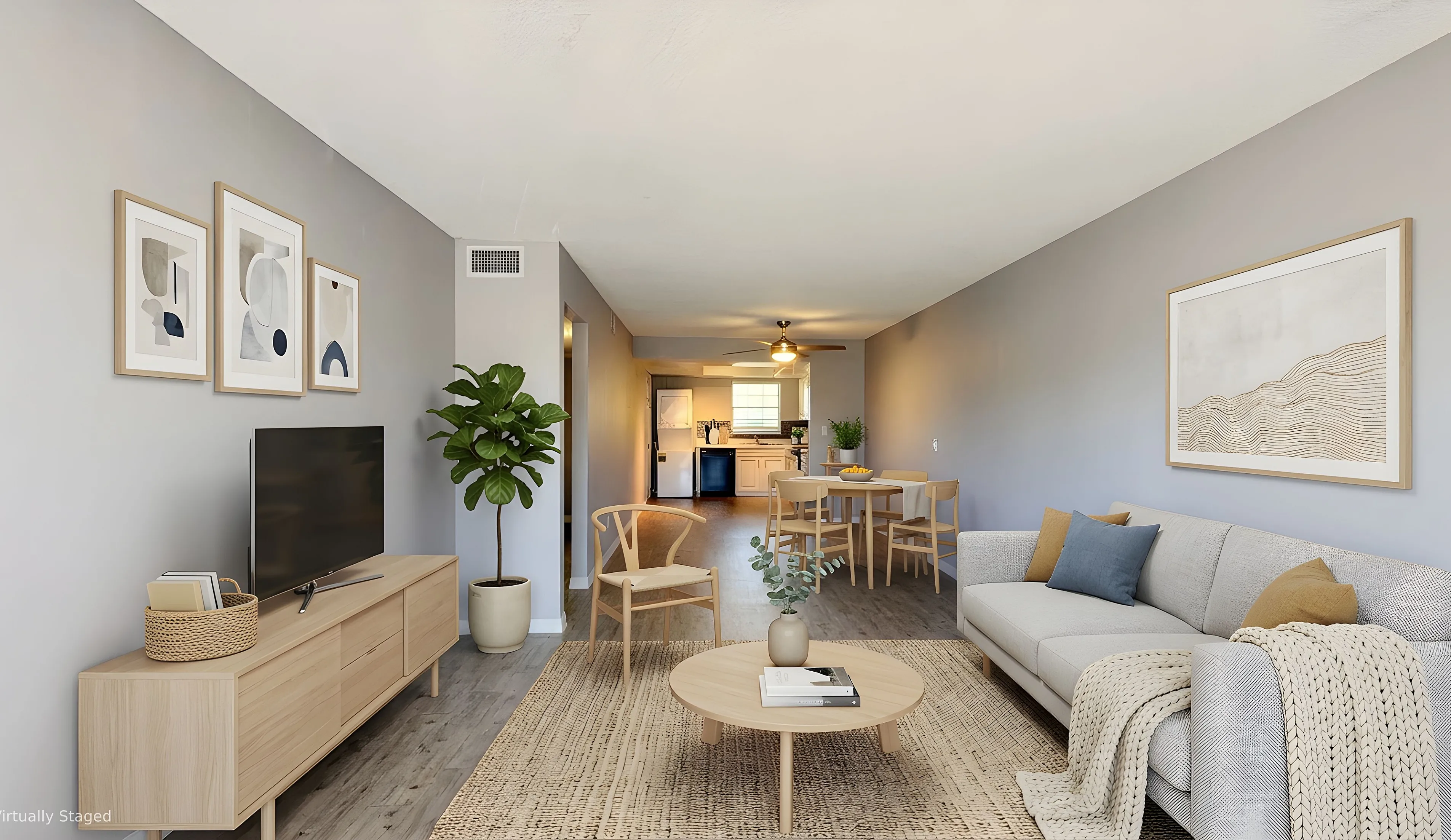 Beautifully staged living room featuring modern decor, cozy gray sofa with accent pillows, stylish wooden furniture, and a glimpse of a contemporary kitchen in an open-concept layout.