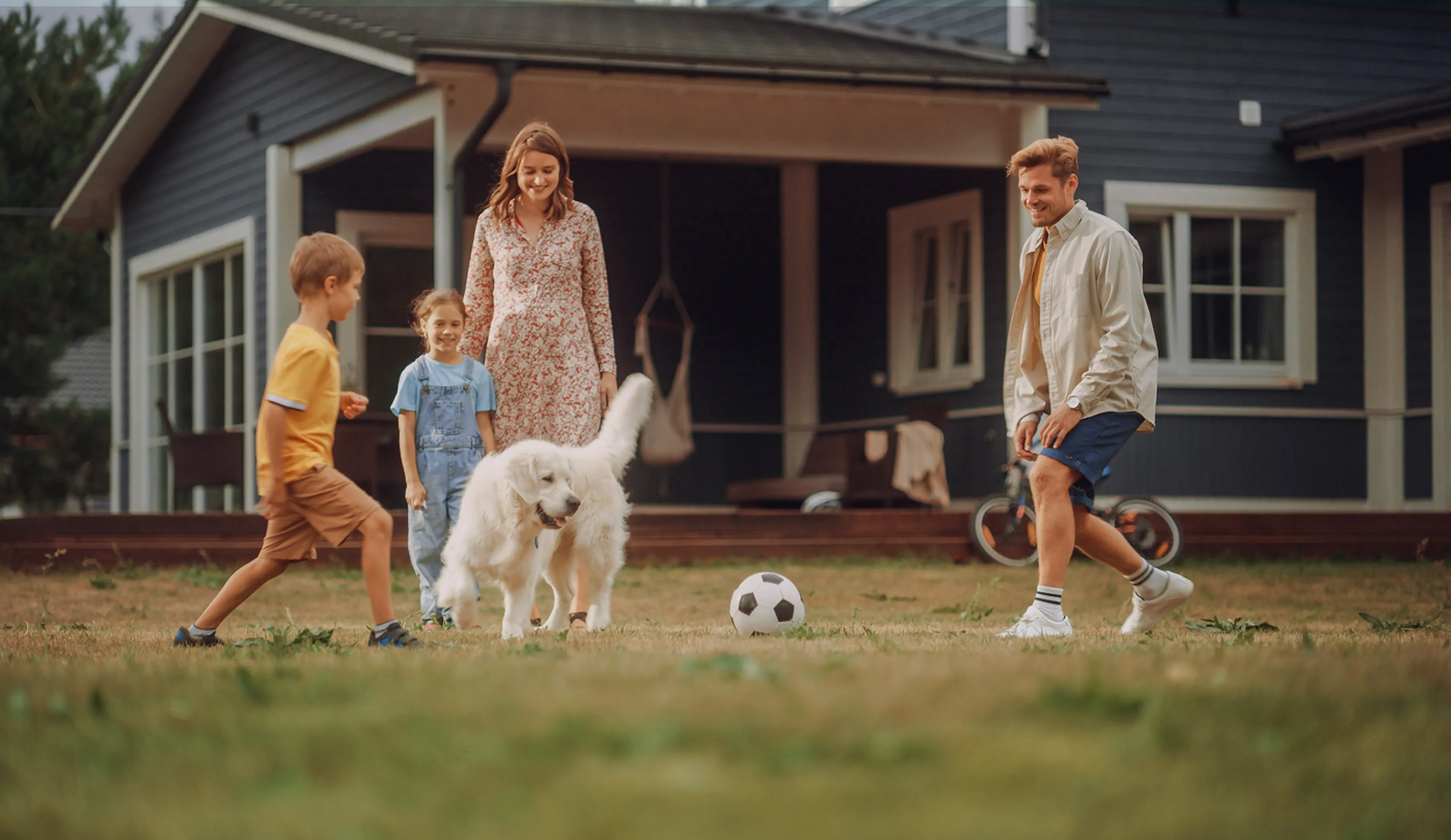 Happy family playing soccer with their dog in front of a charming suburban home.
