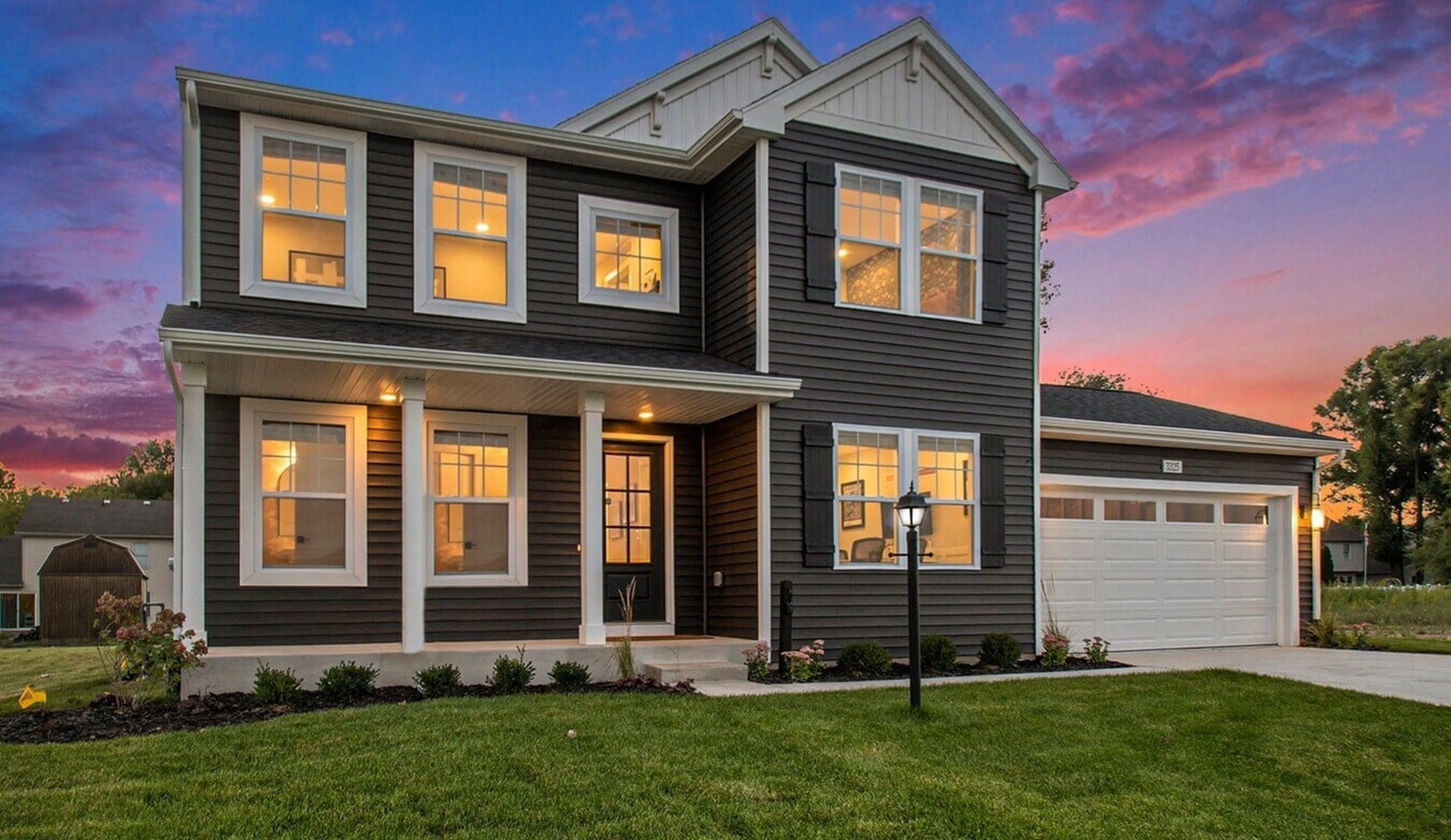 Elegant two-story home with large windows, a welcoming porch, and a spacious two-car garage, set against a breathtaking sunset sky.