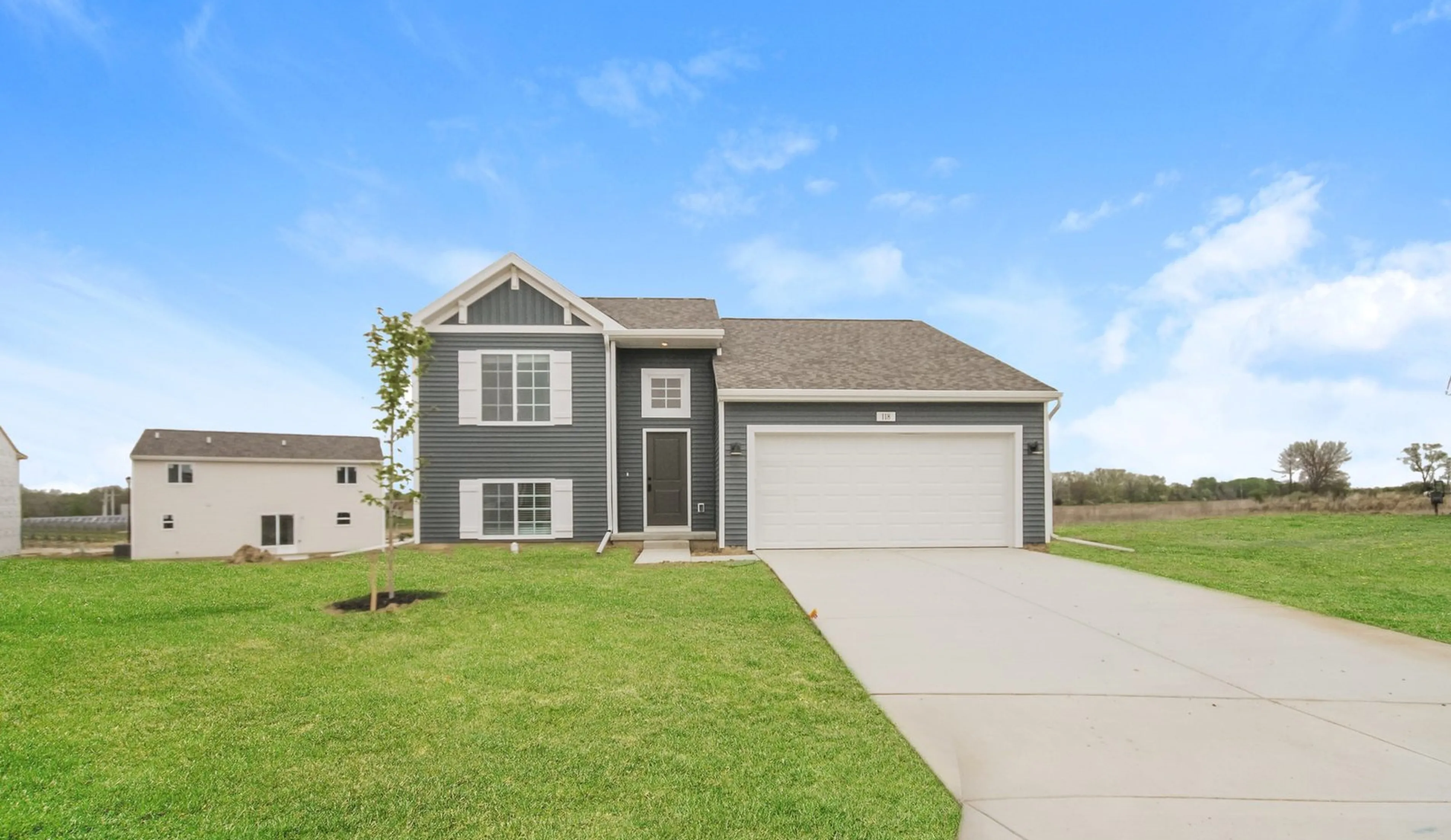 Charming single-family home with a modern grey facade, spacious two-car garage, and lush green lawn set against a serene blue sky.