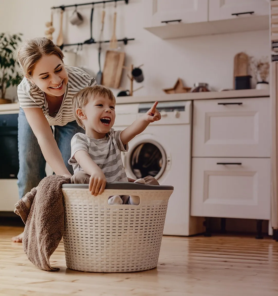 Bright and cheerful modern kitchen with a happy child in a laundry basket, exuding warmth and family joy.