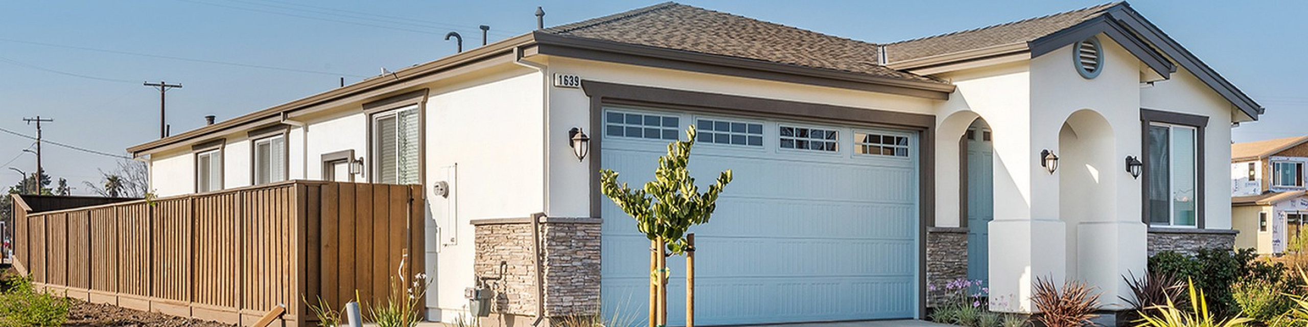 Modern single-story home with a sleek design, featuring a spacious two-car garage, elegant stone accents, and a beautifully landscaped front yard under a clear blue sky.