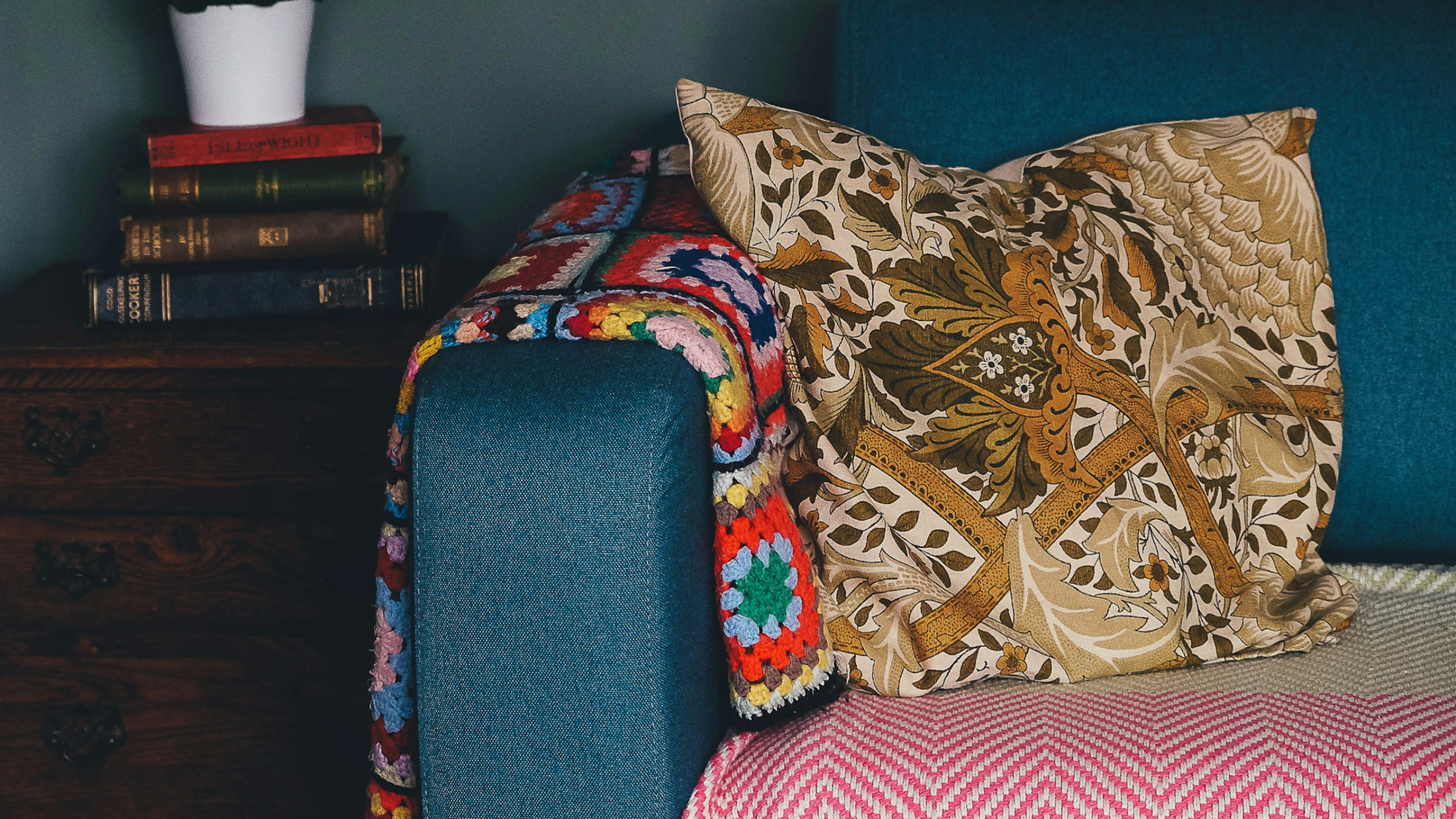 Cozy living space with a vibrant crochet blanket, decorative pillow, and elegant wooden furniture adorned with classic books.